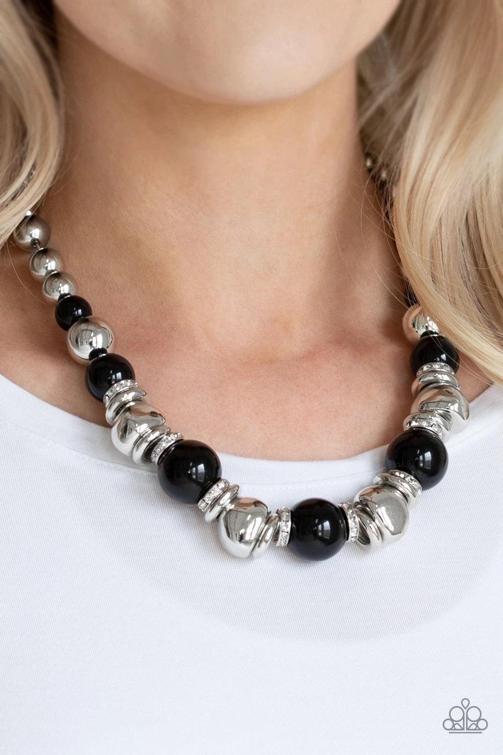 Paparazzi Accessories Hollywood HAUTE Spot - Black A collection of oversized shiny black, silver rings, and asymmetrical silver beads are threaded along an invisible wire below the collar. White rhinestone encrusted rings are sprinkled between the refined