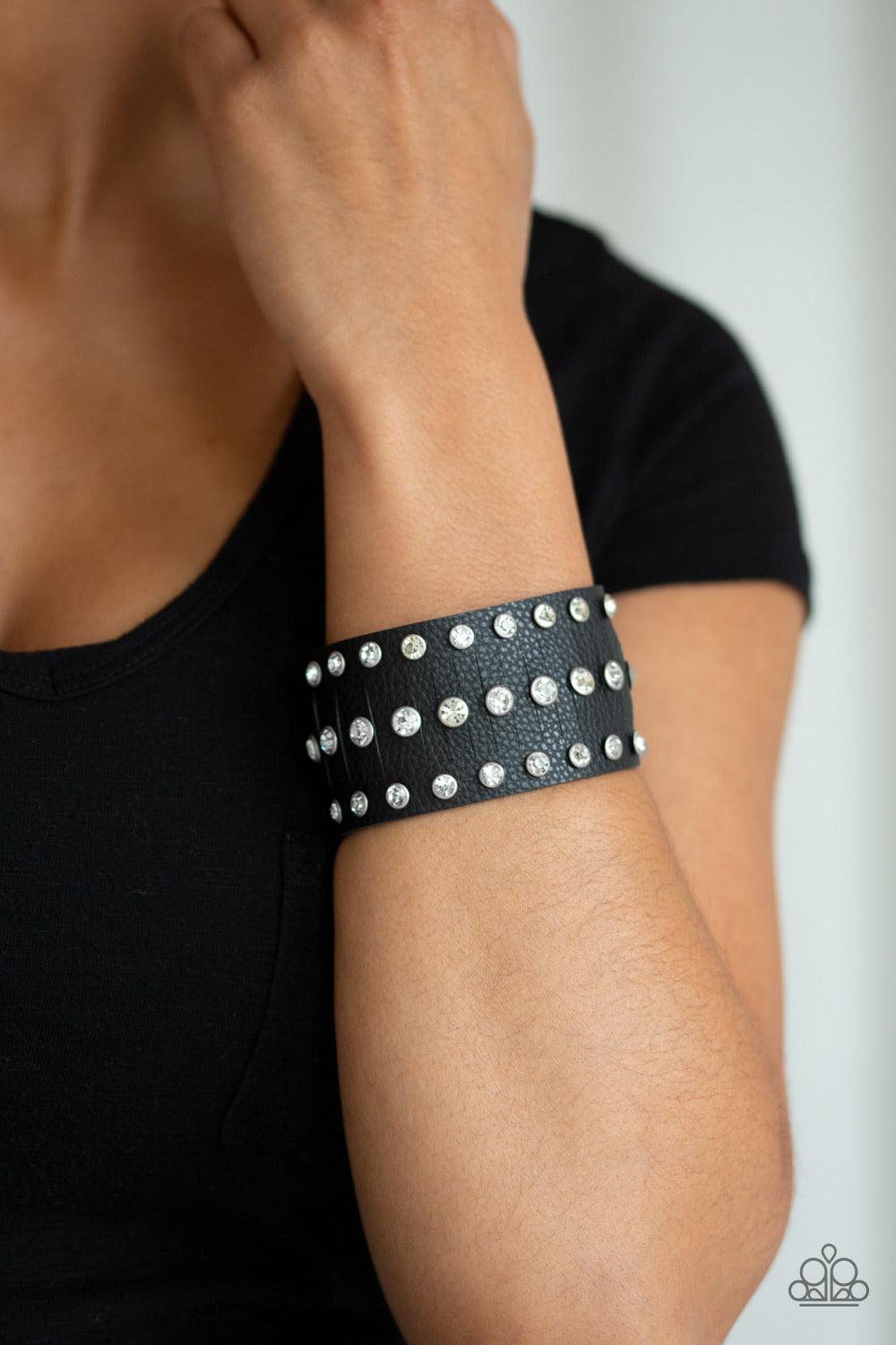 Paparazzi Accessories Now Taking The Stage - Black Pressed into sleek silver frames, glittery white rhinestones are studded across a thick black leather band featuring a center lined with slits for a sassy finish. Features an adjustable snap closure. Sold