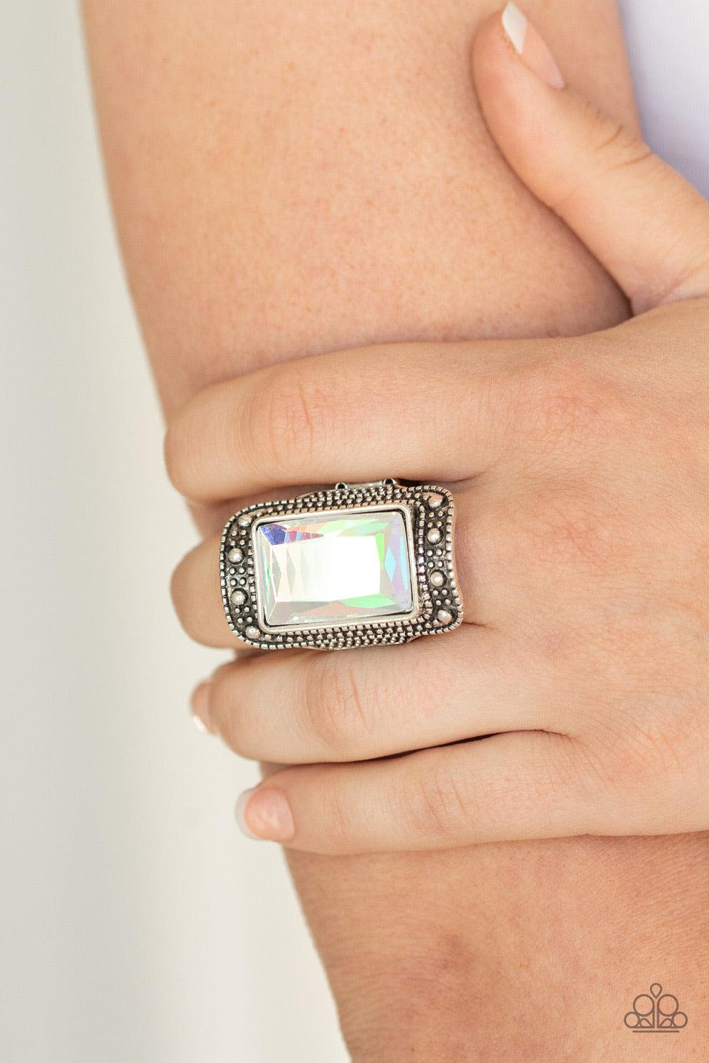 Paparazzi Accessories Very HEIR-descent ~White Featuring an iridescent oil spill finish, a dramatic emerald-cut gem is pressed into the center of a studded silver frame for a jaw-dropping look. Features a stretchy band for a flexible fit.
