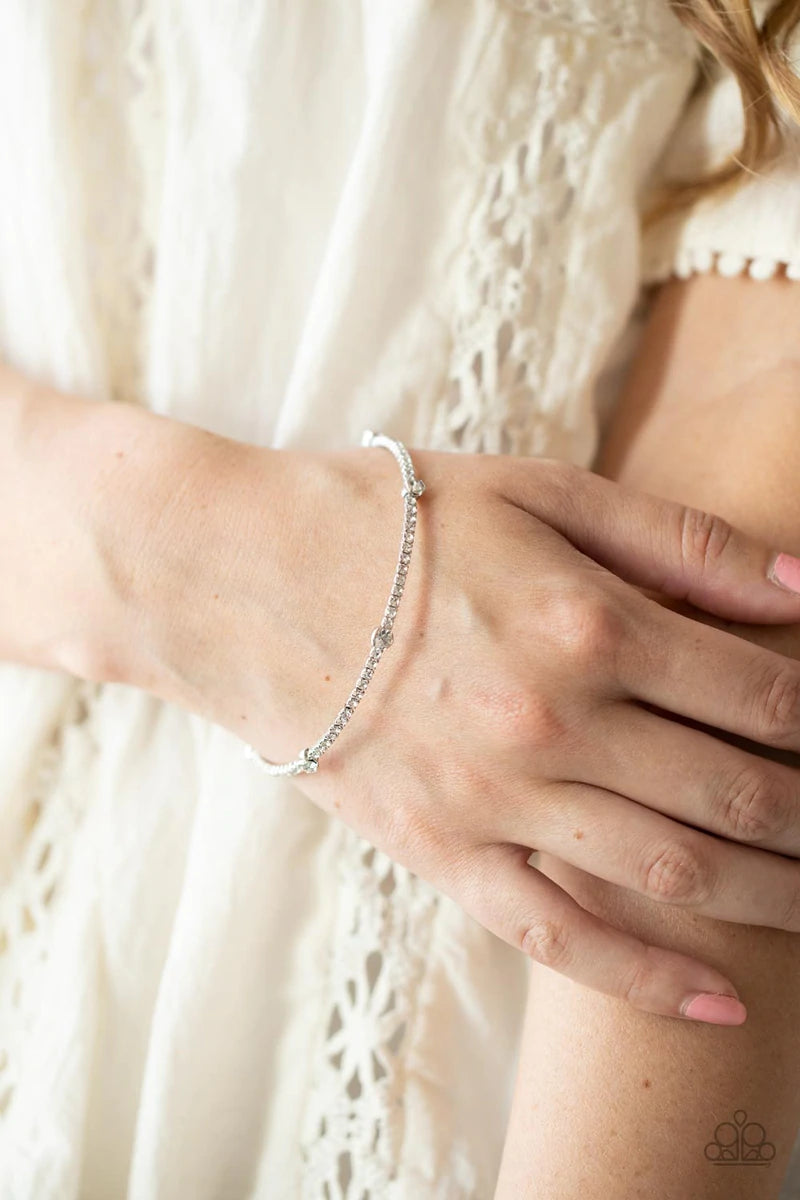 Paparazzi Accessories Upgraded Glamour - White Encased in shiny silver fittings, a sparkly collection of solitaire white rhinestones adorn a glittery strand of dainty white rhinestones that coil around the wrist, creating a dainty cuff. Sold as one indivi