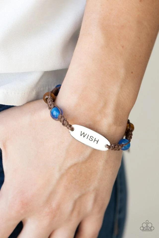 Paparazzi Accessories WISH This Way - Blue An oval silver plate engraved with the word "WISH" creates a warmhearted medallion as it connects to brown cording interwoven with wooden and glossy blue beads for a harmonious vibe around the wrist. Features an