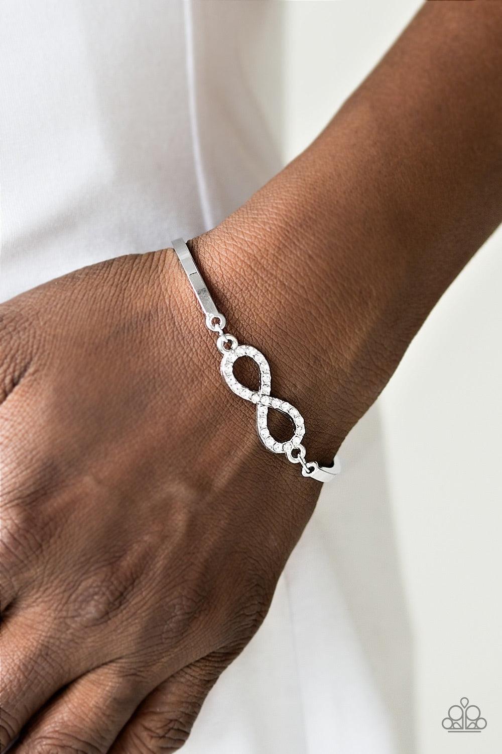 Paparazzi Accessories Infinite Treasure - White Two arching silver bars are separated by a shimmery infinity charm. Encrusted with dainty white rhinestones, the dainty charm delicately links with the silver bars, creating the illusion of a floating center