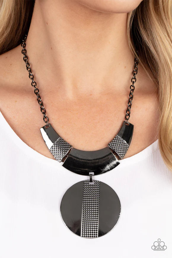 Paparazzi Accessories Metallic Enchantress - Black Three curved gunmetal bars, stamped in studded texture accents, connect to a gunmetal chain across the collar. An oversized gunmetal disc, divided down the center with texture, swings from the bottom resu