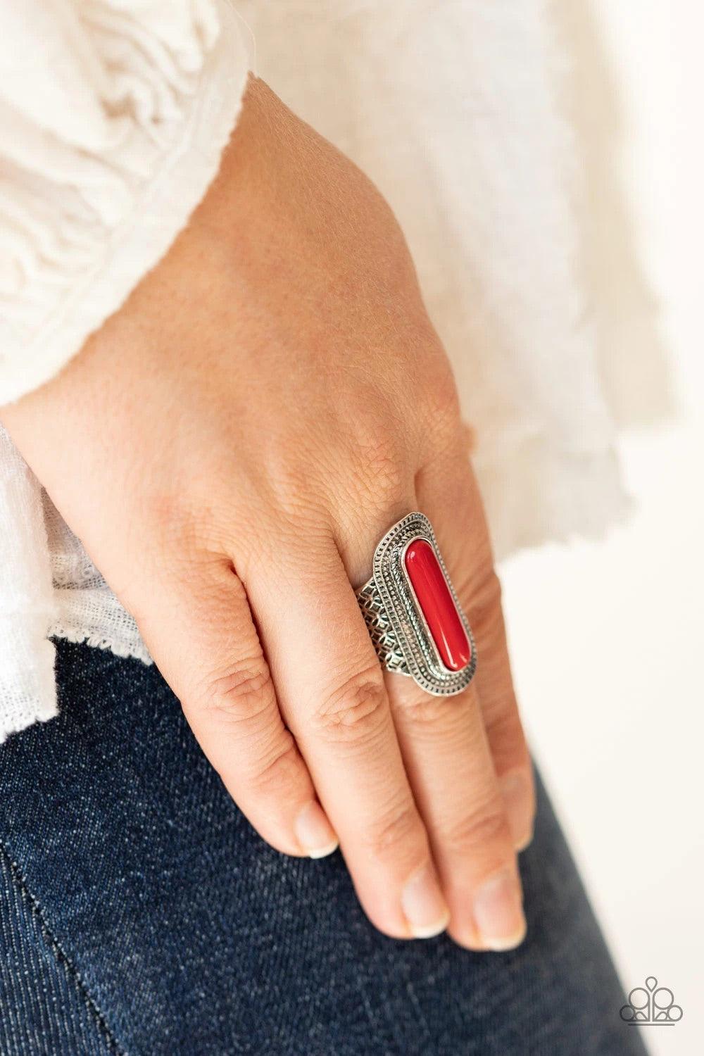 Paparazzi Accessories Dubai Distraction - Red An oblong red bead adorns the center of an oval silver frame studded and stamped in tactile texture. The radiant frame attaches to a silver band embossed in antiqued floral-like details, creating a colorful ce