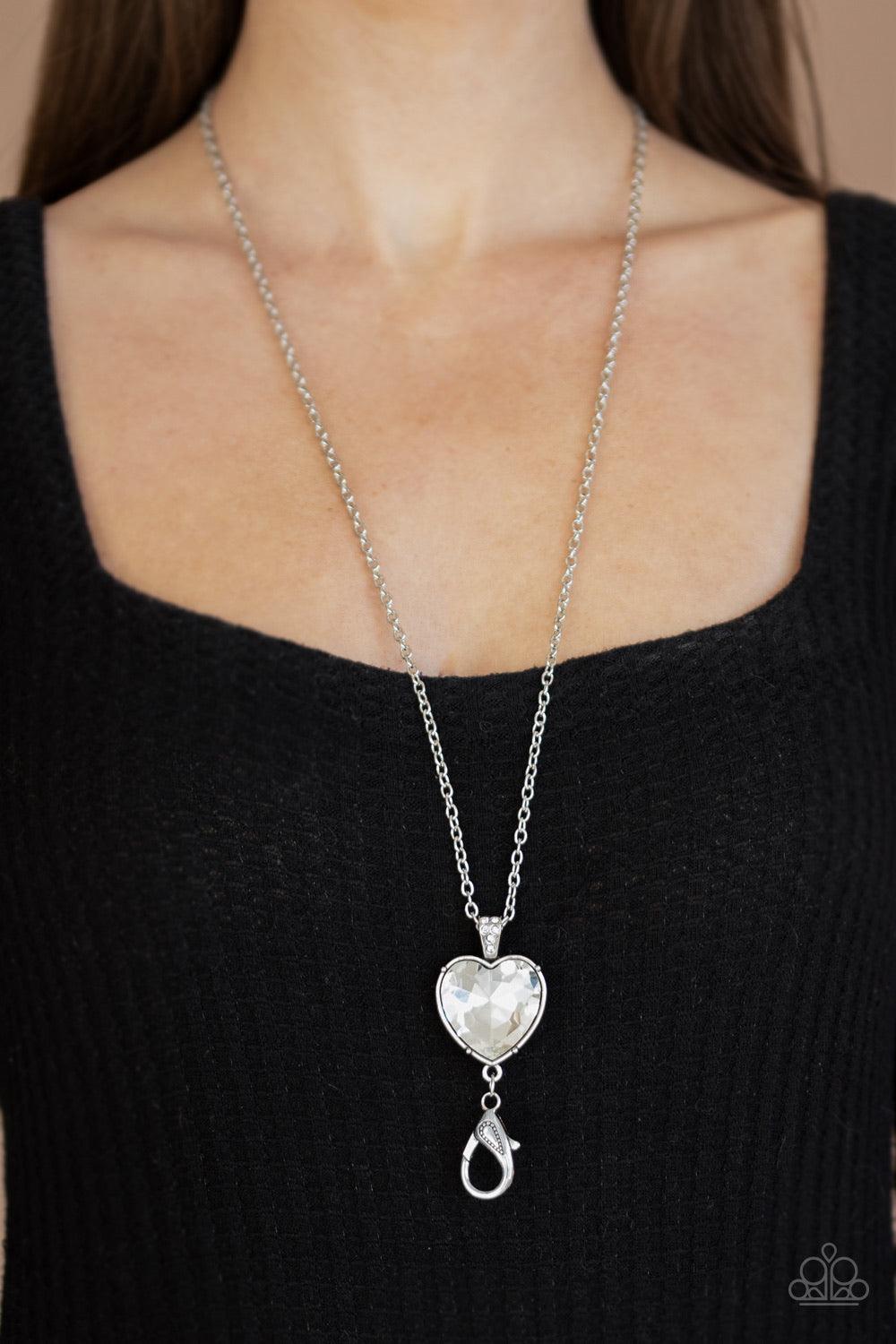 Paparazzi Accessories Lovely Luminosity - Silver *Lanyard Attached to a white rhinestone encrusted fitting, an oversized heart cut gem pendant swings from the bottom of a shimmery silver chain for a charming look. A lobster clasp hangs from the bottom of