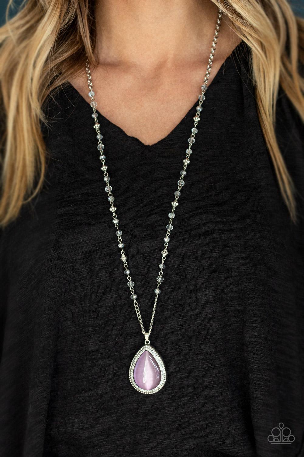 Paparazzi Accessories Fashion Flaunt - Purple Encrusted in rows of glassy white rhinestones, an imperfect silver teardrop frame is encrusted in a glowing purple cat's eye stone. The ethereal pendant swings from the bottom of a lengthened silver chain dott