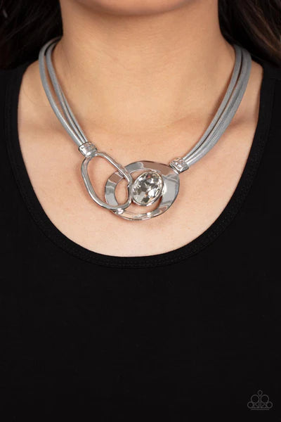Paparazzi Accessories Californian Cowgirl - Silver Attached to shimmery strands of silver leather, a pair of oversized and warped silver links delicately overlaps into a contemporary centerpiece below the collar. An exaggerated white gem asymmetrically em