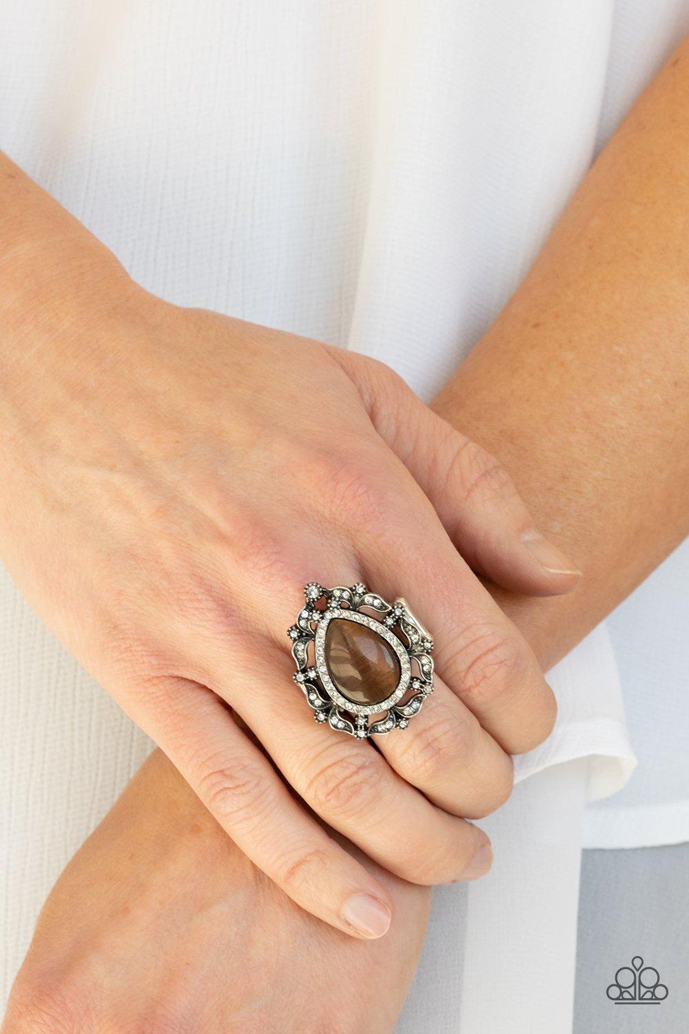 Paparazzi Accessories Iridescent Icy - Brown Dotted in glittery white rhinestones, leafy silver frames nestle around a glowing brown cat's eye teardrop center, creating a regal centerpiece atop the finger. Features a stretchy band for a flexible f Jewelry