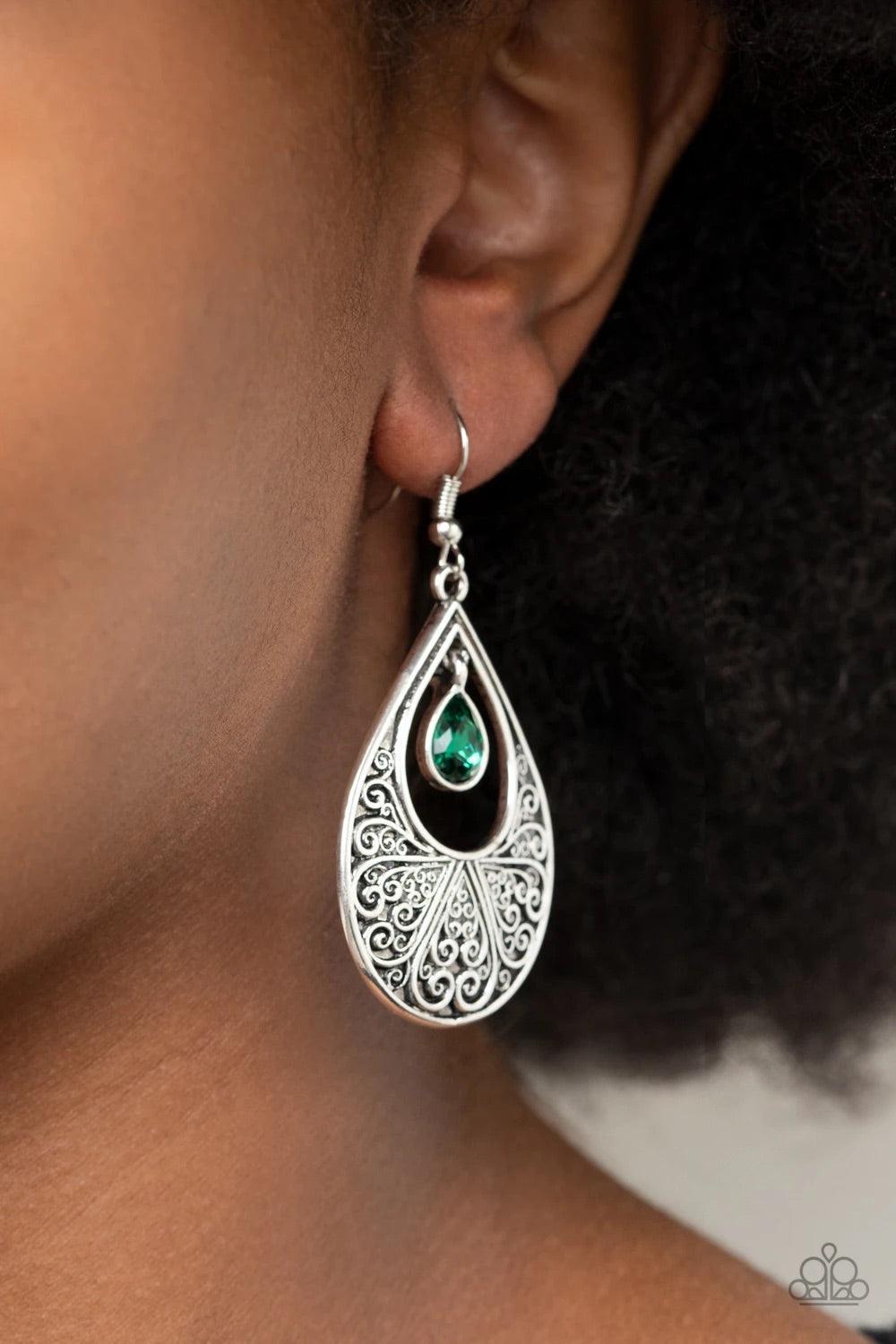 Paparazzi Accessories Garden Magic - Green A glassy green rhinestone swings from the top of an airy silver teardrop frame embossed with heart-shaped filigree, creating a whimsical lure. Earring attaches to a standard fishhook fitting. Sold as one pair of
