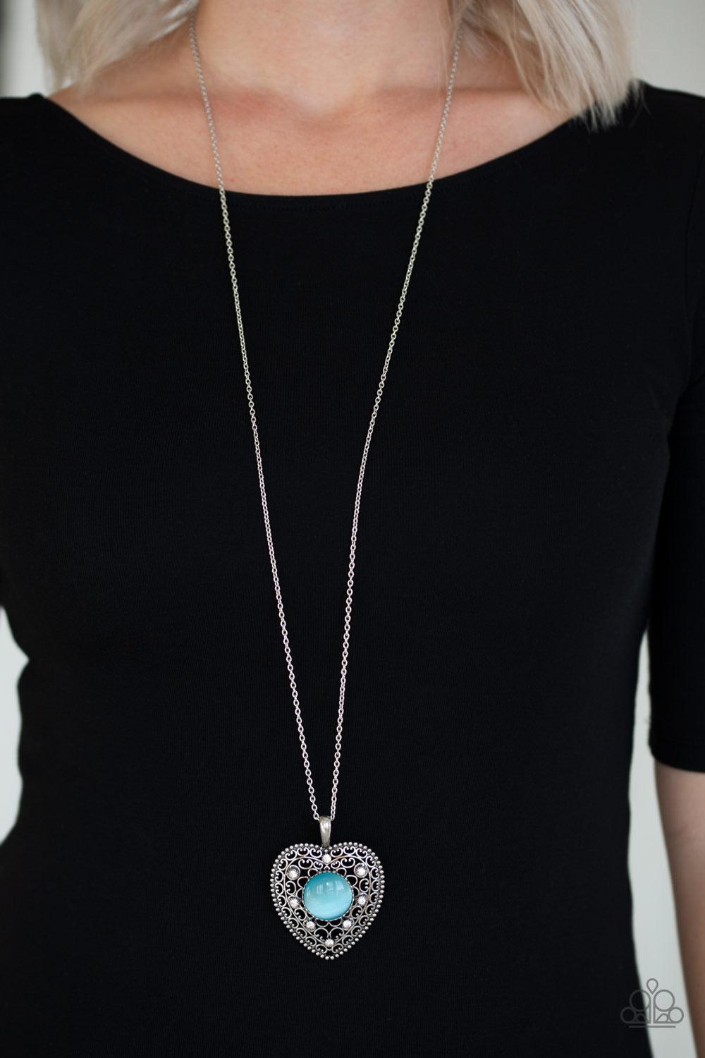 Paparazzi Accessories One Heart - Blue Featuring a glowing blue moonstone center, an oversized heart frame radiating with silver filigree and glittery white rhinestones swings from the bottom of a lengthened silver chain for a whimsical look. Features an