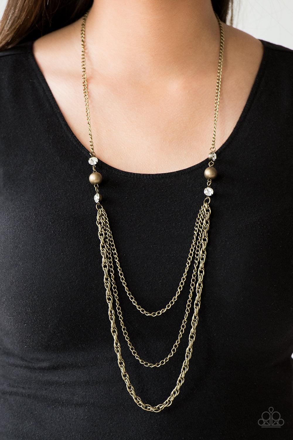 Paparazzi Accessories RITZ it All - Brass Glittery white rhinestones and oversized brass beads give way to layers of mismatched brass chains for a refined look. Features an adjustable clasp closure. Jewelry