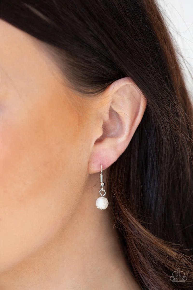 Paparazzi Accessories Medallion Meadow - White Swinging from the bottom of a lengthened silver chain, a refreshing white stone is pressed into a hammered silver medallion radiating with floral details for a bold tribal inspired look. Features an adjustabl