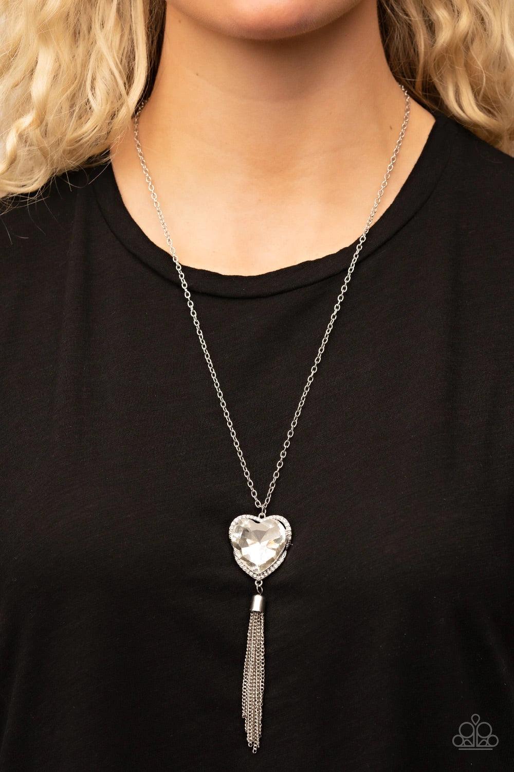 Paparazzi Accessories Finding My Forever - White Bordered in a ribbon of glassy white rhinestones, an oversized white heart-shaped gem seemingly floats at the bottom of an extended silver chain. A shimmery silver chain tassel dances from the bottom of the