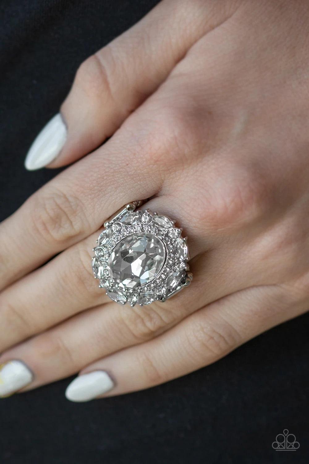 Paparazzi Accessories Show Glam - White An oversized oval white gem is pressed into the center of a round silver frame encrusted in mismatched white rhinestones for a glamorous look. Features a stretchy band for a flexible fit. Sold as one individual ring