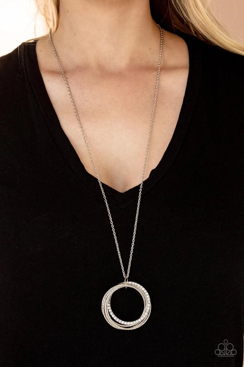 Paparazzi Accessories Harmonic Halos ~White An interconnected collection of shiny silver, textured, and white rhinestone encrusted rings link into a melodic pendant at the bottom of a lengthened silver chain. Features an adjustable clasp closure. Sold as