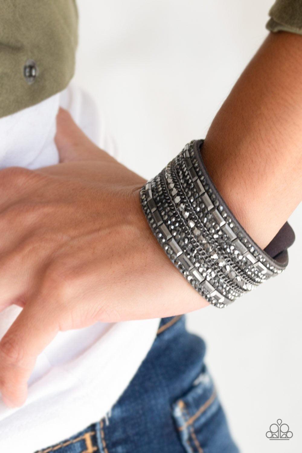 Paparazzi Accessories Rebel Radiance - Silver Featuring classic round and edgy emerald style cuts, glittery hematite rhinestones and glistening gunmetal chains are encrusted along bands of gray suede for a sassy look. Features an adjustable snap closure.