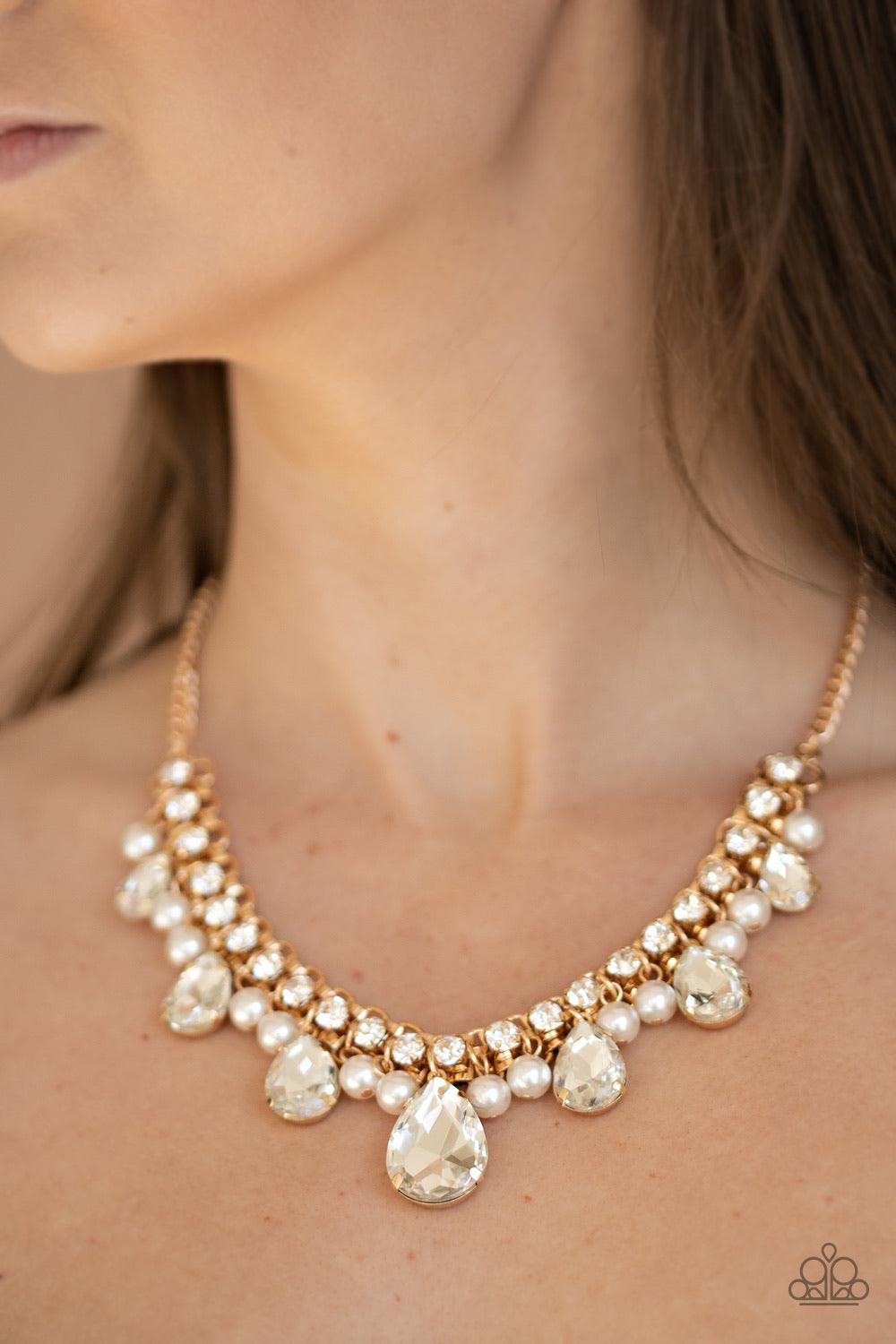 Paparazzi Accessories Knockout Queen - Gold A glamorous collection of bubbly white pearls and exaggerated white teardrop gems dangle from a bold strand of white rhinestones, creating a knockout fringe below the collar. Features an adjustable clasp closure