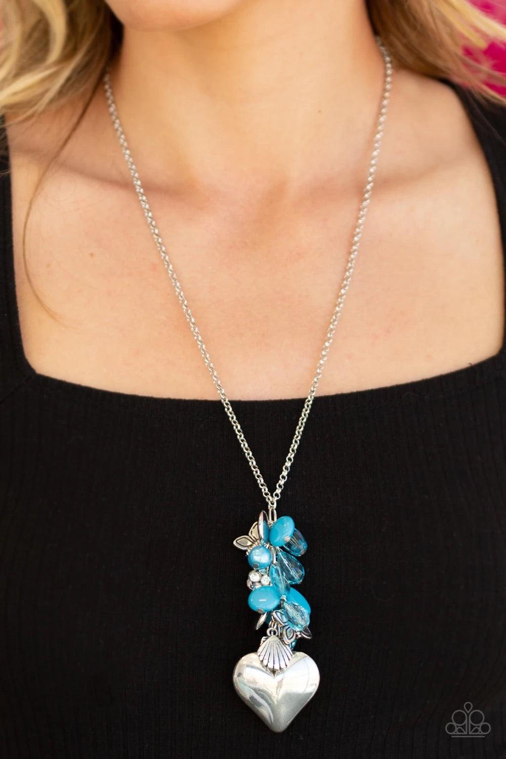 Paparazzi Accessories Beach Buzz - Blue Infused with an array of blue beads, a collection of antiqued silver shell and butterfly charms trickle along the bottom of a shimmery silver chain. Complemented with glittery white rhinestone encrusted beads, a dra