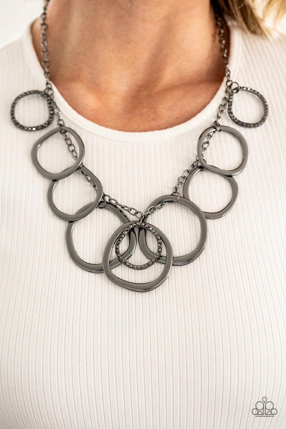 Paparazzi Accessories Dizzy With Desire - Black Oversized asymmetrical gunmetal rings swing from the bottom of a glistening gunmetal chain. Encrusted in hematite rhinestones, matching gunmetal rings trickle between a dizzying fringe, adding a sparkly smol