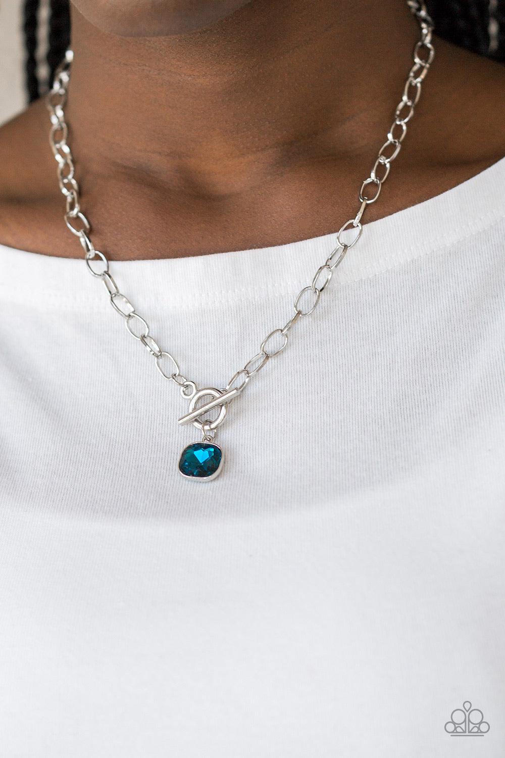 Paparazzi Accessories Dynamite Dazzle - Blue Pressed into a sleek silver frame, a dramatic blue gem swings from the bottom of a glistening silver chain below the collar for a chic look. Features a toggle closure. Jewelry