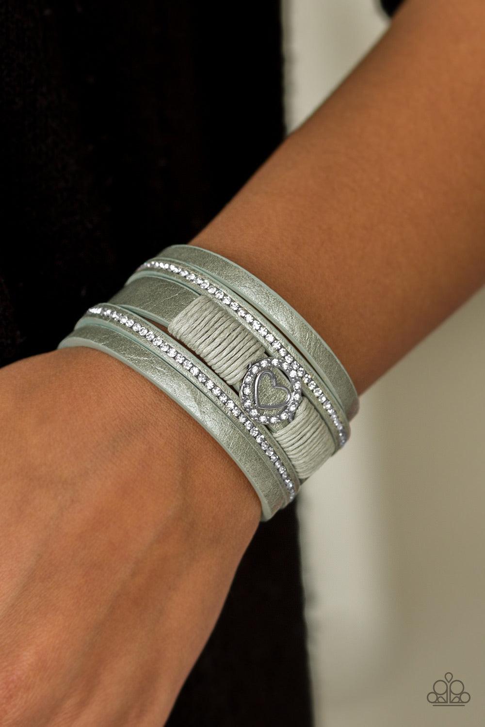 Paparazzi Accessories It Takes Heart - Green Brushed in a metallic shimmer, strips of green leather are encrusted in alternating rows of glittery white rhinestones. Green cording knots around the centermost strand, securing a sparkling heart frame in plac