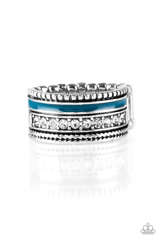 Paparazzi Accessories Rich Rogue - Blue A shiny blue strip of color runs along the bottom of a row of glassy white rhinestones. Infused with silver textures, the mismatched details coalesce into one thick band across the finger. Features a stretchy band f