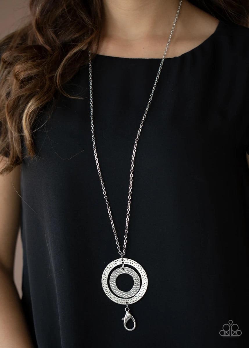 Paparazzi Accessories Circle Back To That - Silver Featuring hammered finishes, two asymmetrical silver rings dangle from the bottom of a lengthened silver chain for a rustic look. A lobster clasp hangs from the bottom of the design to allow a name badge