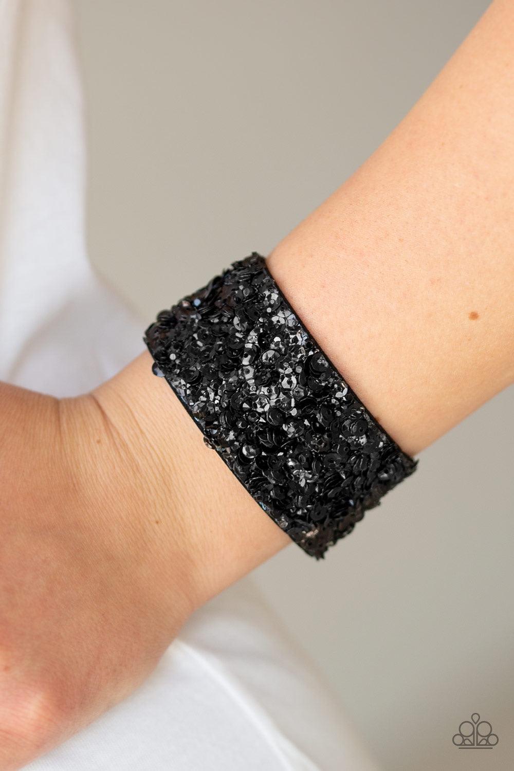 Paparazzi Accessories Starry Sequins - Black A collision of glittery black rhinestones and sparkling black sequins are encrusted along the front of a black suede band, creating blinding shimmer around the wrist. Features an adjustable snap closure. Jewelr