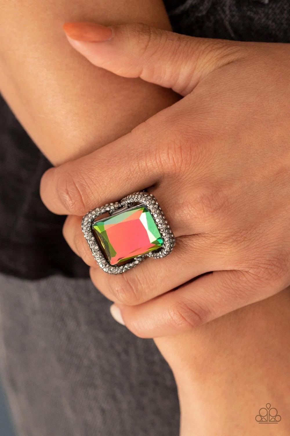 Paparazzi Accessories Deluxe Decadence - Multi Featuring a regal emerald style cut, an oversized oil spill gem nestles inside a rounded square gunmetal frame encrusted in smoky hematite rhinestones for a dramatically glamorous look. Features a stretchy ba