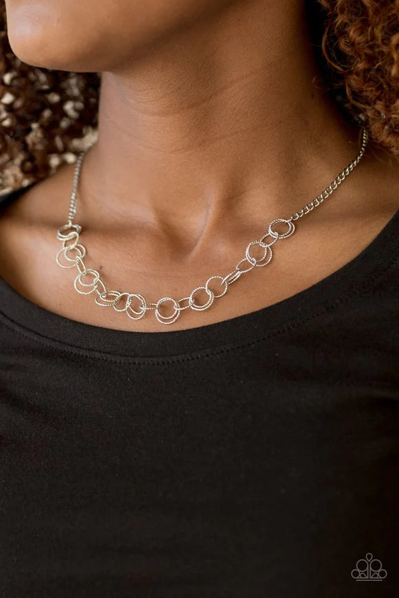Paparazzi Accessories One RING Leads To Another - Silver Delicately etched in radiant textures, dainty silver rings join below the collar in a dizzying fashion. Features an adjustable clasp closure. Sold as one individual necklace. Includes one pair of ma