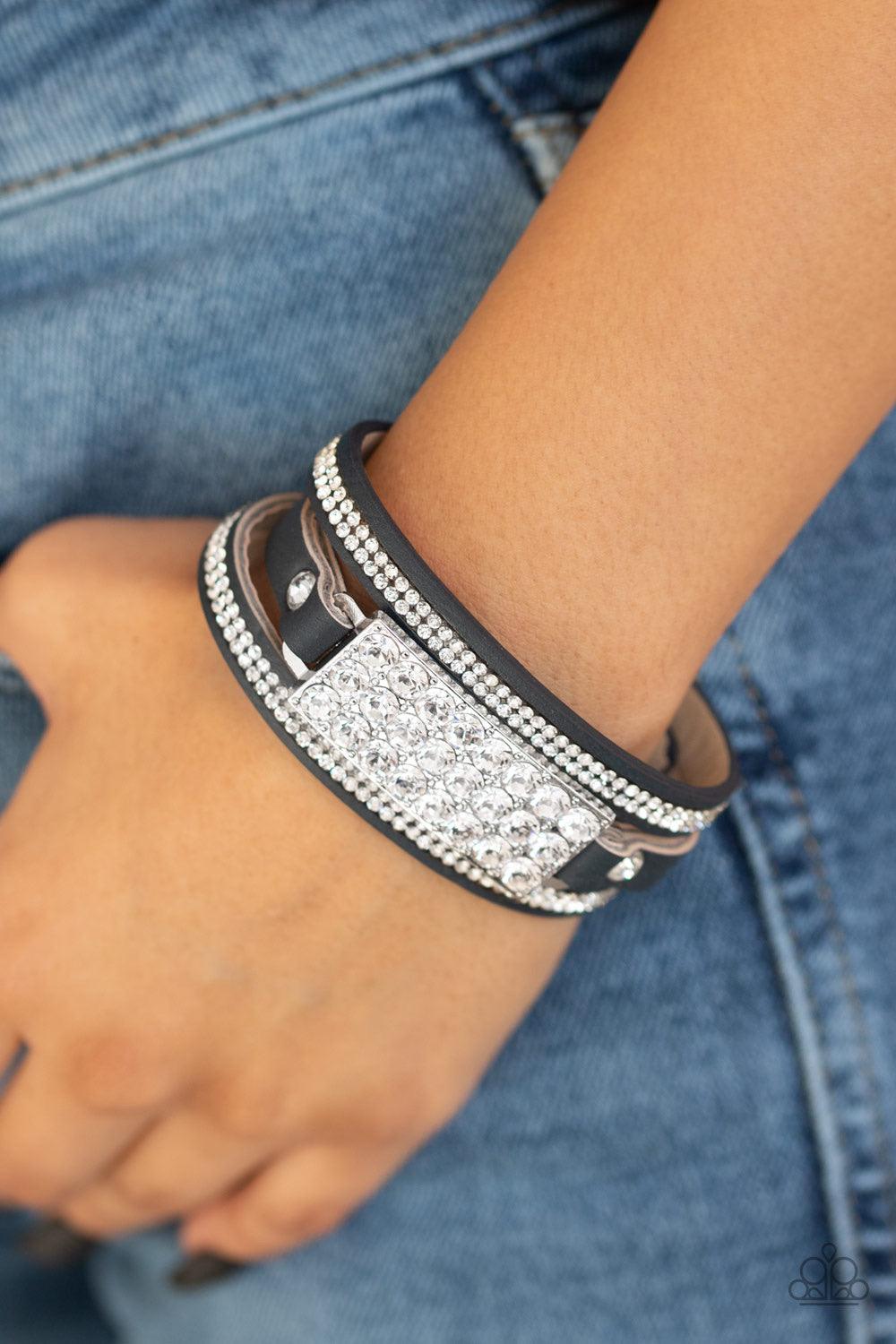 Paparazzi Accessories Shockingly Sparkly - Black A thick blue leather band is spliced into three separate strands. Encrusted in rows of glassy white rhinestones, two glittery strands flank a blinding silver buckle encrusted in oversized white rhinestones