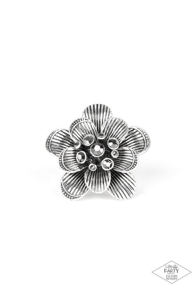 Paparazzi Accessories Petal Pusher - Silver Engraved in linear patterns, antiqued silver petals bloom into an oversized floral frame atop the finger. A bouquet of glittery hematite rhinestones burst from the center, creating a sparkling statement piece at