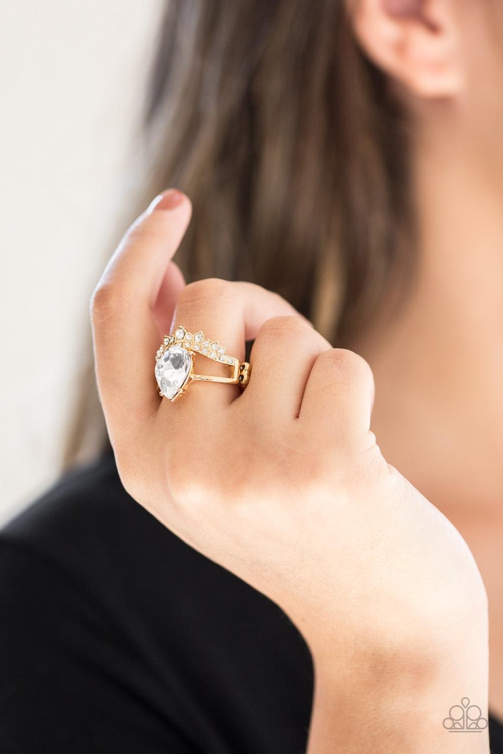 Paparazzi Accessories If the Crown Fits - Gold A shiny gold bar and white rhinestone encrusted bar arc across the finger, coalescing into an airy band. Featuring a regal teardrop cut, a glittery white rhinestone is pressed into the bands for a statement m