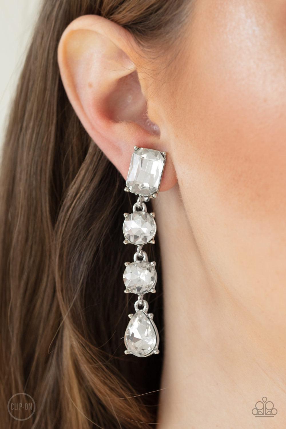 Paparazzi Accessories Make A-List ~White *Clip-On Featuring a glassy white finish, a collection of emerald, round, and teardrop cut rhinestones drip from the ear, connecting into a glamorous lure. Earring attaches to a standard clip-on fitting. Sold as on