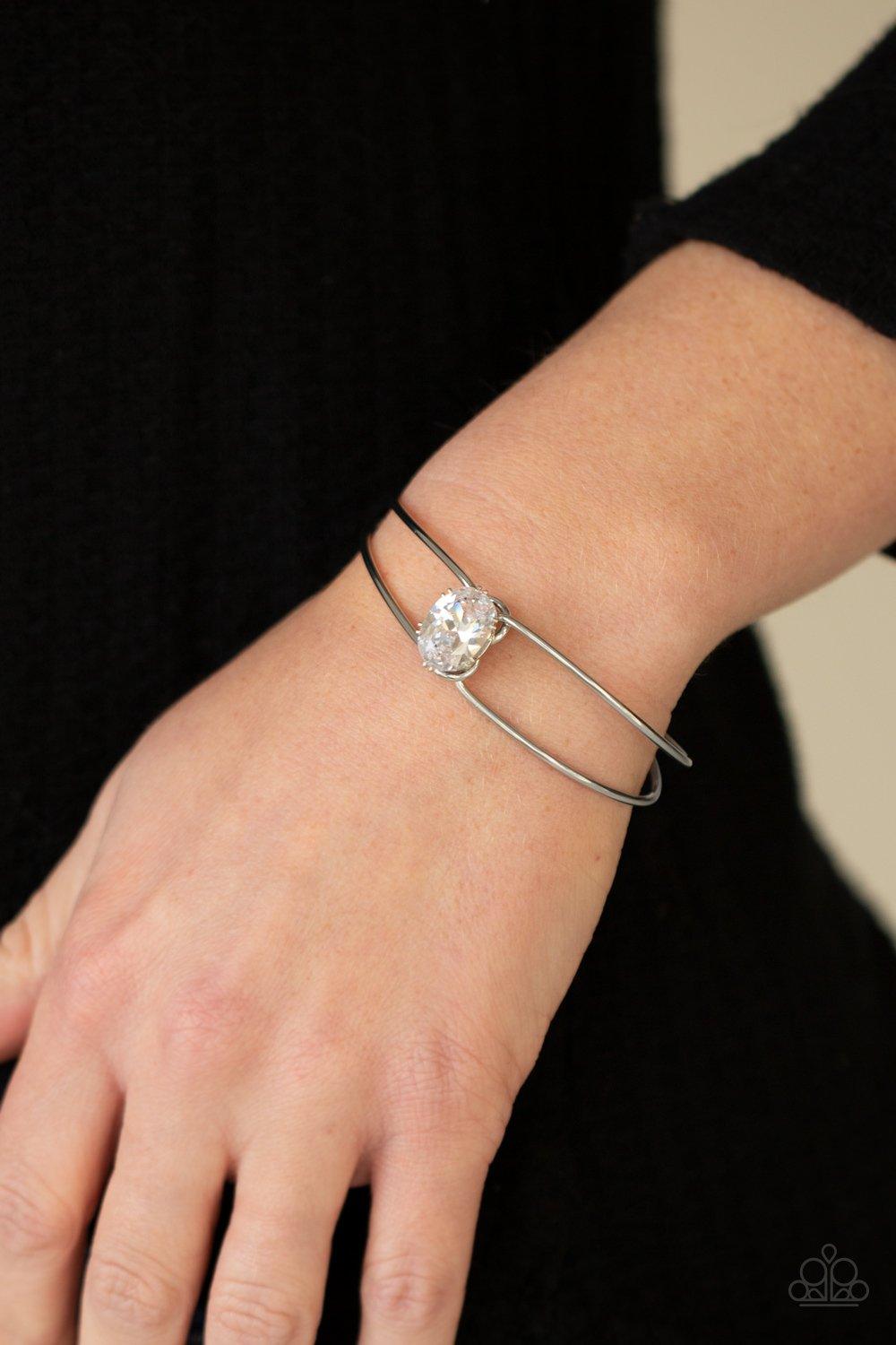 Paparazzi Accessories GLOW No Mercy - White A dramatically oversized white rhinestone is fitted in place atop the center of a silver wire cuff, creating a jaw-dropping display around the wrist. Sold as one individual bracelet. Jewelry