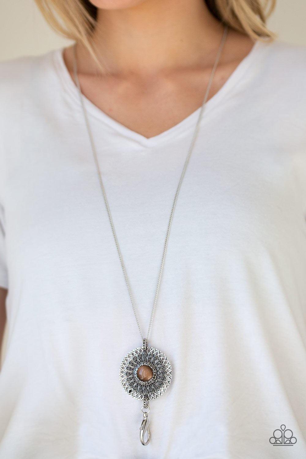 Paparazzi Accessories So Solar - Brown *Lanyard A glowing brown moonstone is pressed into the center of a silver medallion radiating with ornate sunburst textures for a whimsical look. A lobster clasp hangs from the bottom of the design to allow a name ba