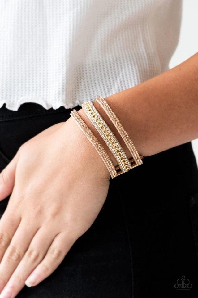 Paparazzi Accessories Rollin In Rhinestones - Gold Rows of glassy peach and white rhinestones and a shimmery gold chain are encrusted along tan suede bands for a sassy look. Features an adjustable snap closure. Jewelry