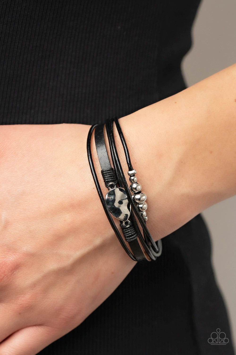 Paparazzi Accessories Tahoe Tourist - Black Infused with a silver beaded accent, rows of shiny black cording join a black leather band around the wrist. A hammered silver teardrop is knotted in place with black thread, adding an artisanal touch to the rus