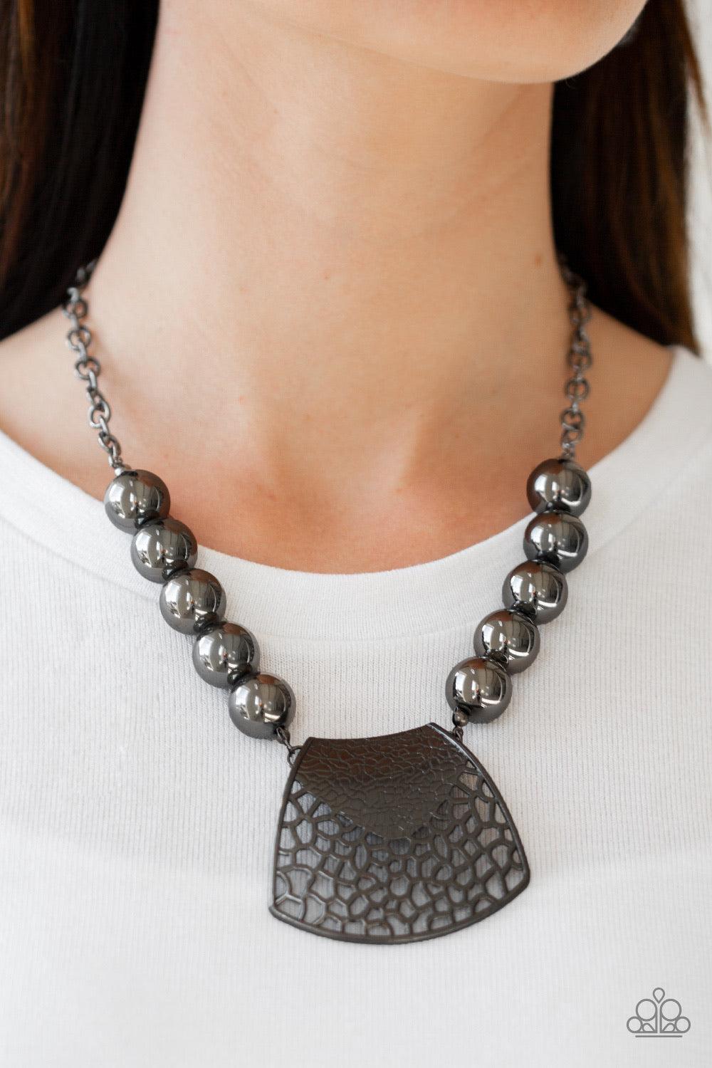 Paparazzi Accessories Large And In Charge - Black Featuring ornately stenciled and embossed details, a flared gunmetal plate swings from a boldly gunmetal beaded chain below the collar for a fierce look. Features an adjustable clasp closure. Sold as one i