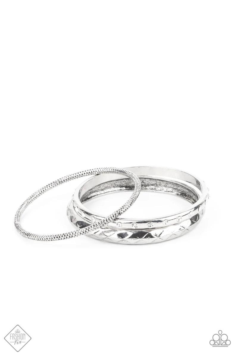 Paparazzi Accessories Confidently Curvaceous - White A thick silver bangle that is embossed and faceted in an edgy geometric pattern joins a mismatched pair of white rhinestone encrusted and diamond cut silver bangles that glide along the wrist, displayin