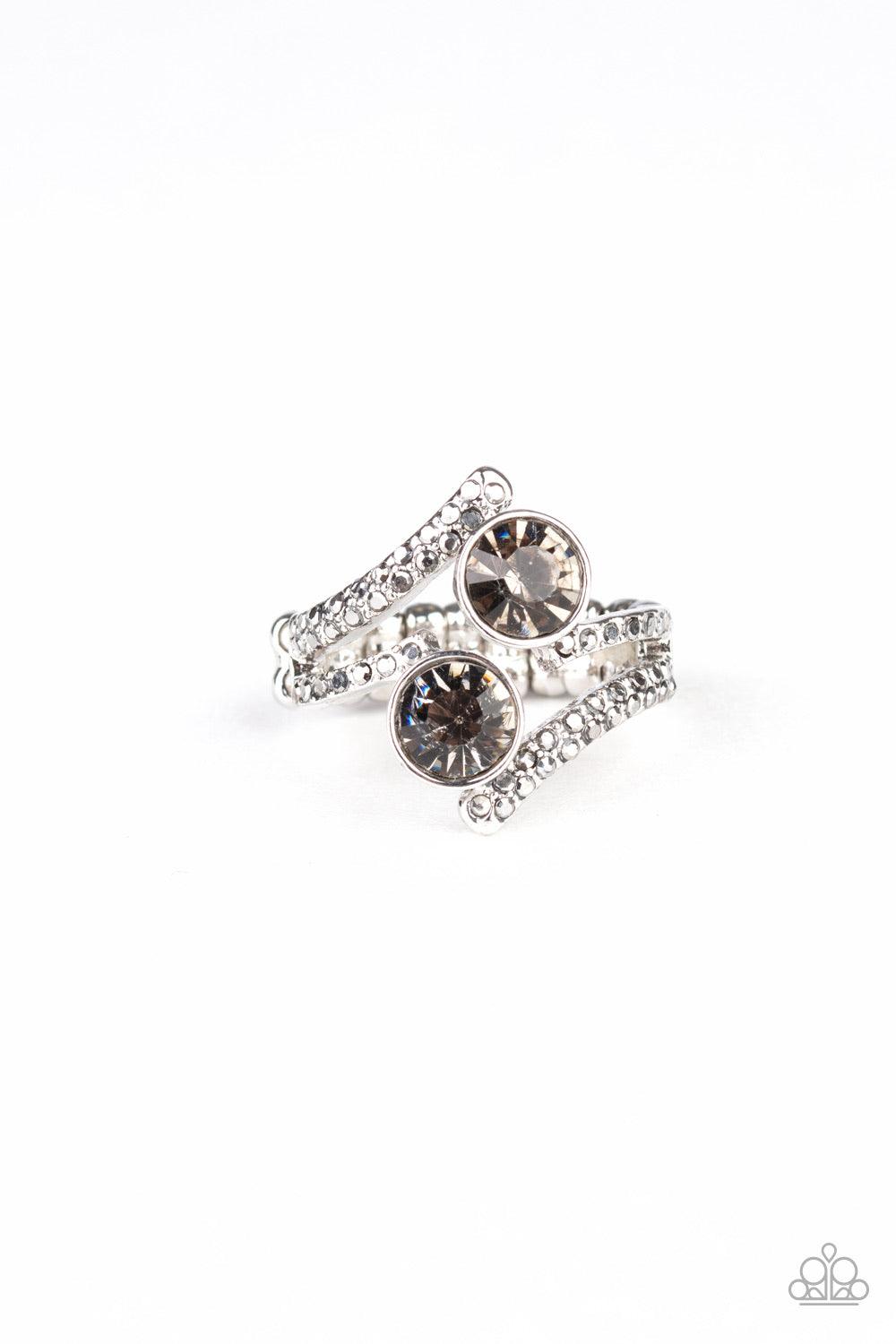 Paparazzi Accessories Over The Top Glamour - Silver Two oversized smoky rhinestones sit atop two zigzagging silver bands encrusted in dainty hematite rhinestones. Features a dainty stretchy band for a flexible fit. Sold as one individual ring. Jewelry