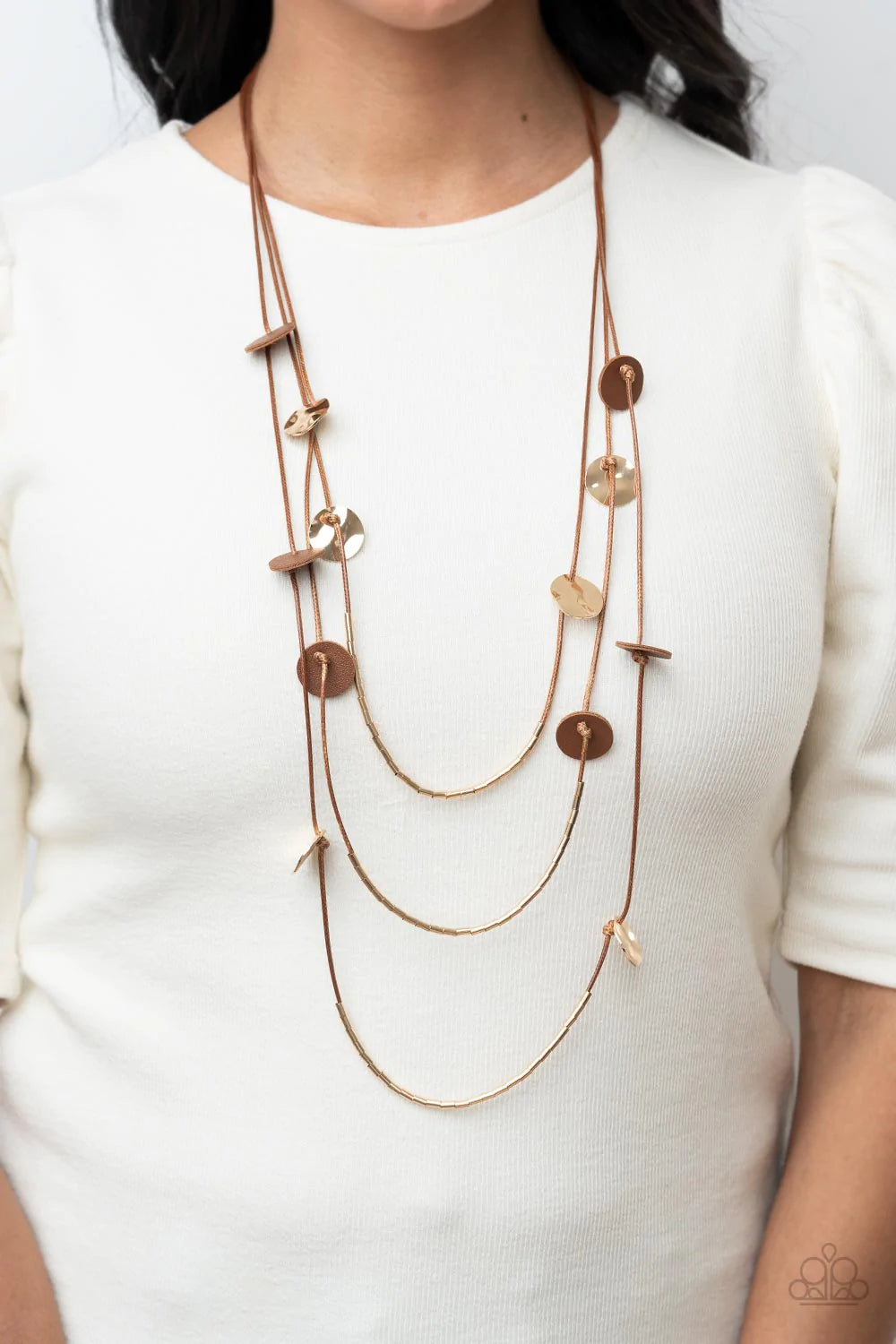Paparazzi Accessories Alluring Luxe - Brown Shining wavy gold discs and brown leather discs adorn a trio of lengthened subtly shimmering brown cords. Rows of dainty gold cylinders are threaded along the bottom of each cord adding luxurious allure to the p