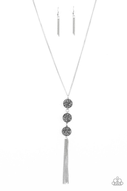 Paparazzi Accessories Triple Shimmer - Silver Sprinkled in smoky and hematite prism style rhinestones, three sparkling silver frames trickle down the chest. A shimmery silver tassel swings from the bottom of the triple stacked pendant for a glamorous fini