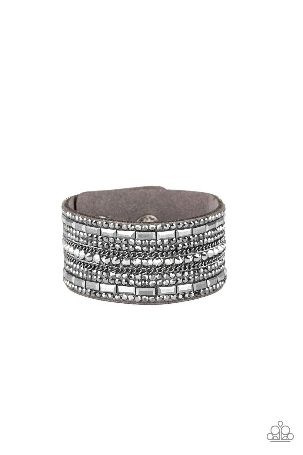 Paparazzi Accessories Rebel Radiance - Silver Featuring classic round and edgy emerald style cuts, glittery hematite rhinestones and glistening gunmetal chains are encrusted along bands of gray suede for a sassy look. Features an adjustable snap closure.