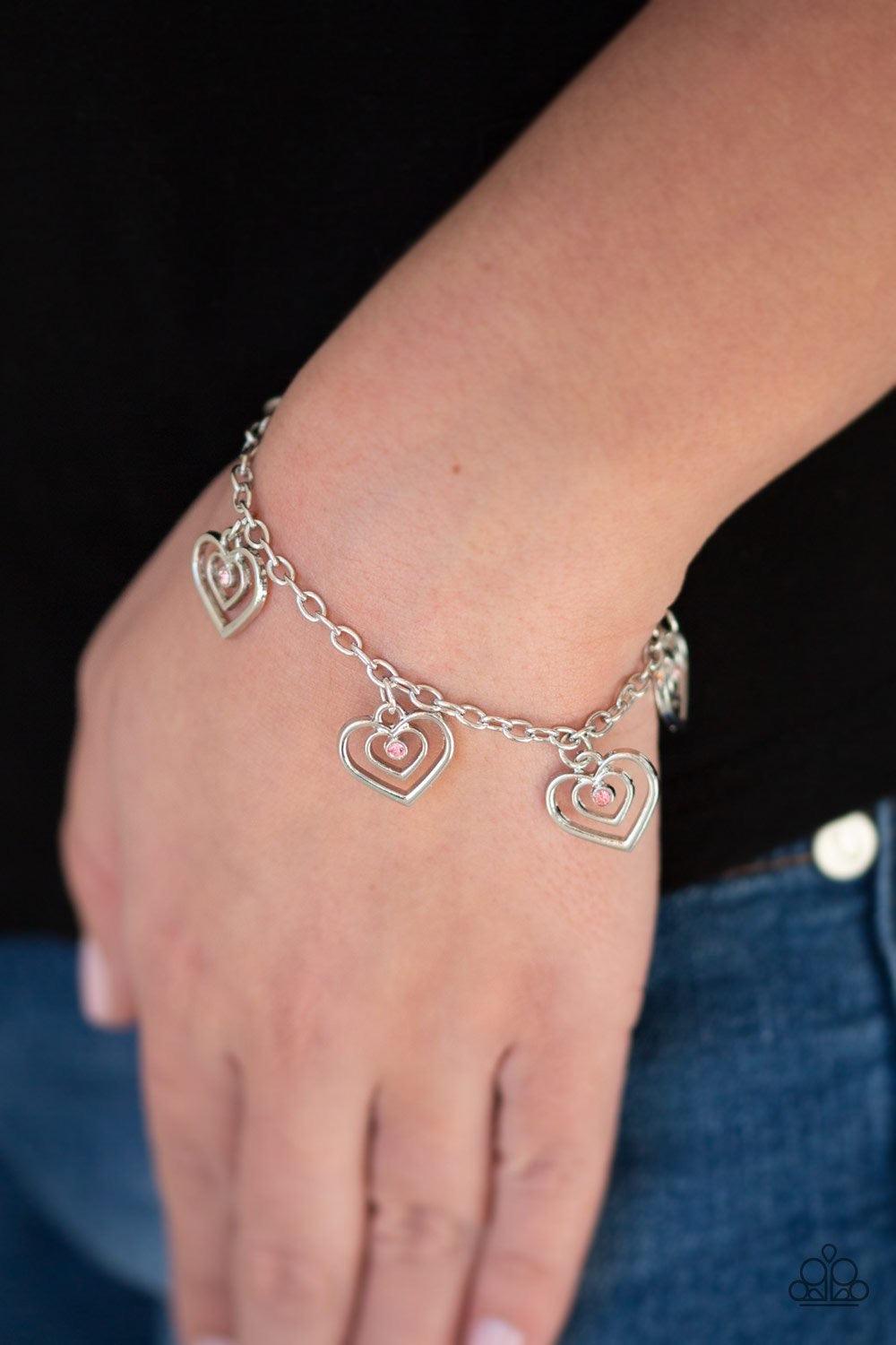 Paparazzi Accessories Unbreakable Hearts ~Pink Dotted with dainty pink rhinestone centers, spiraling silver heart chains swing from the wrist for a flirty look. Features an adjustable clasp closure. Sold as one individual bracelet.