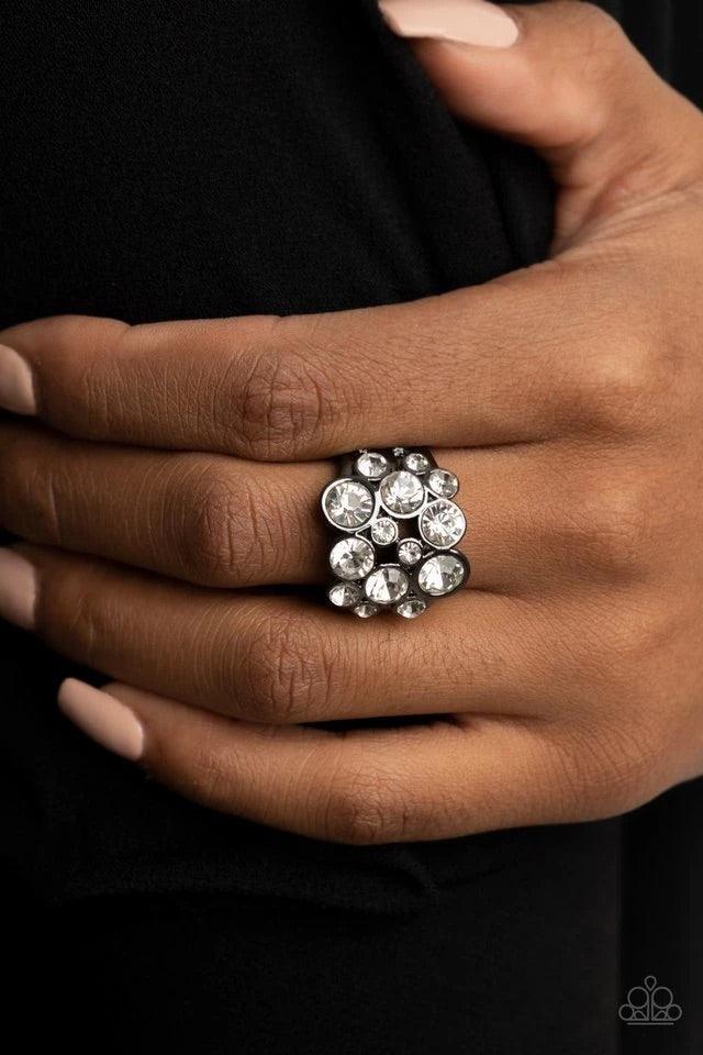 Paparazzi Accessories Bubbling Bravado - Black Encased in sleek gunmetal frames, a bubbly collection of sparkly white rhinestones coalesces into a glamorous band across the finger. Features a stretchy band for a flexible fit. Jewelry