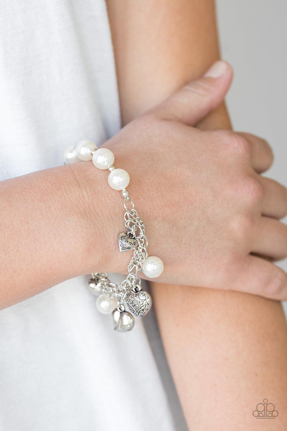 Paparazzi Accessories More Amour - White Attached to a section of shimmery silver chain, pearly white and dainty silver beads are threaded along a stretchy band. Mismatched silver heart charms swing from the glistening chain, creating a flirty fringe. Jew