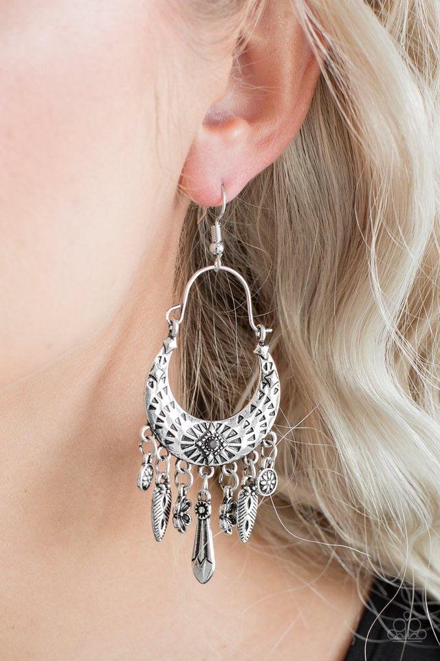 Paparazzi Accessories Nature Escape ~Silver Stamped in triangular textures, a shimmery silver crescent frame gives way to a fringe featuring glistening floral and abstract charms. Suspended by a dainty wire fitting, the tribal inspired frame is dotted wit