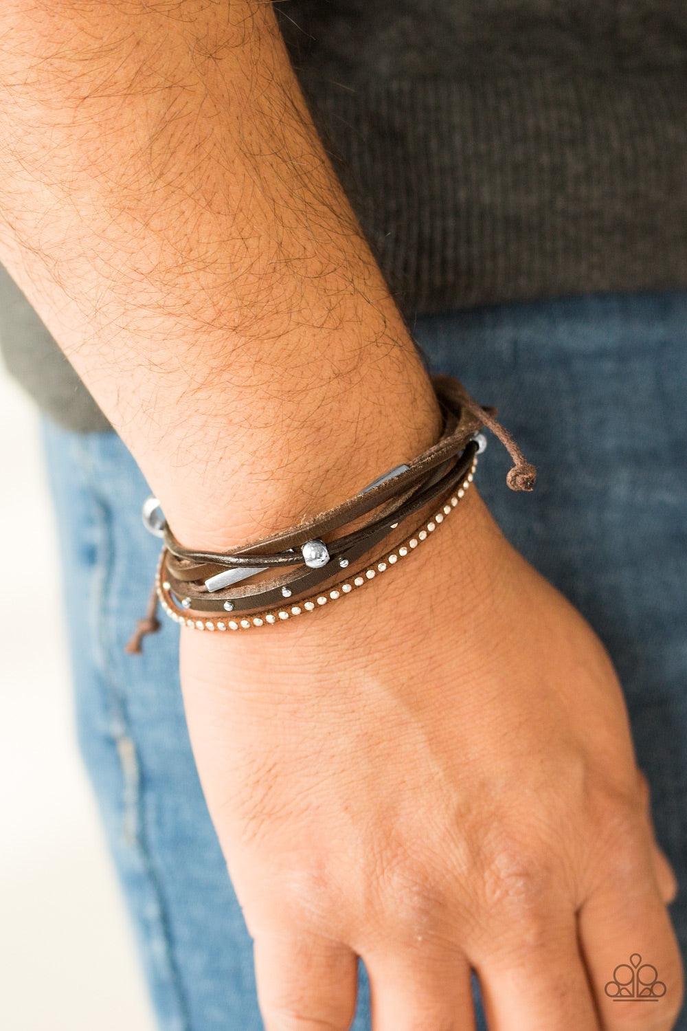 Paparazzi Accessories Long Road Home - Brown A mishmash of skinny leather bands and shiny brown cording layer across the wrist. Featuring mismatched studded textures and shiny metallic accents, a single wooden bead slides along the brown cord for an urban
