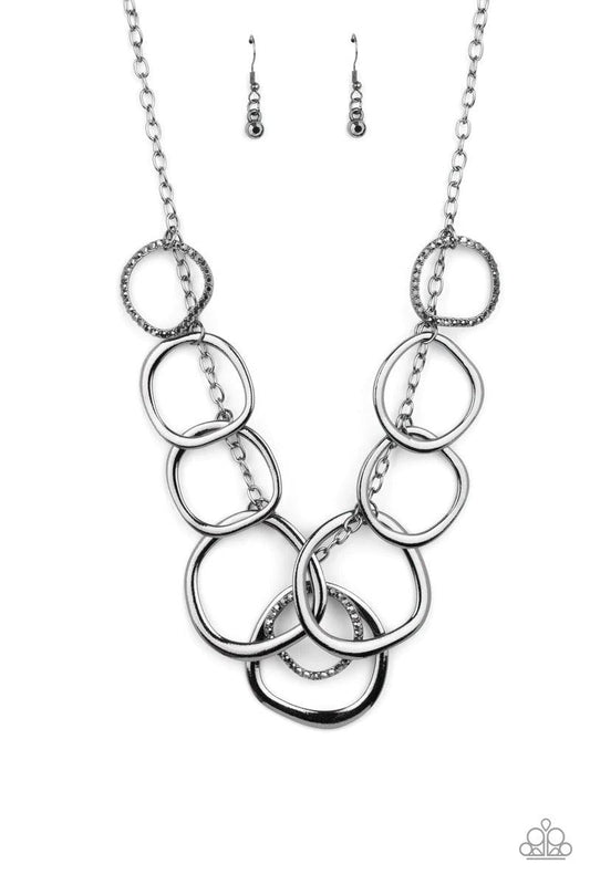 Paparazzi Accessories Dizzy With Desire - Black Oversized asymmetrical gunmetal rings swing from the bottom of a glistening gunmetal chain. Encrusted in hematite rhinestones, matching gunmetal rings trickle between a dizzying fringe, adding a sparkly smol